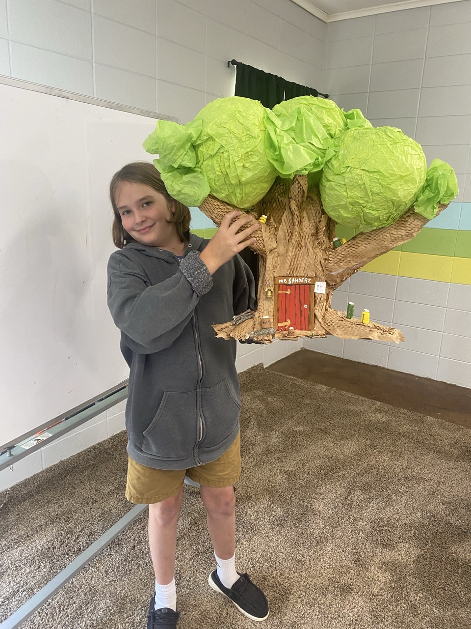 A student holding a handmade treehouse model for a literature project