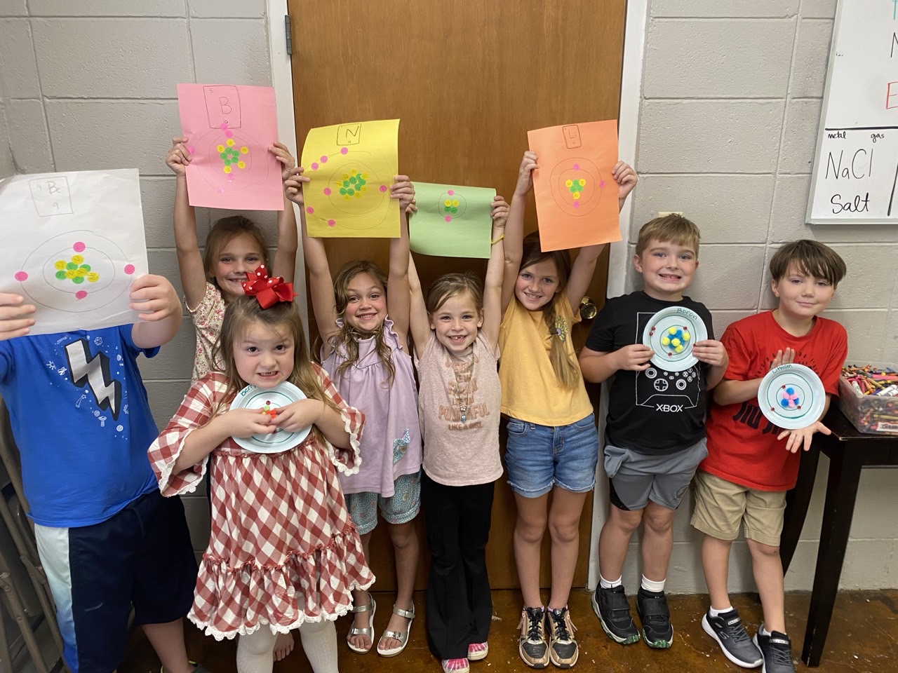 Younger students holding up their atom model art projects